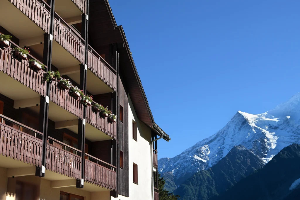 Fachada de alojamiento alpino con balcones de madera y vistas a las montañas nevadas del Pirineo Aragonés, ideal para casas rurales en el Pirineo Aragonés.